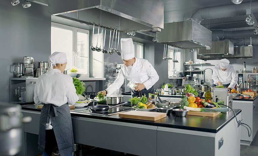 A woman and two men in chef's clothes at work in a commercial kitchen.